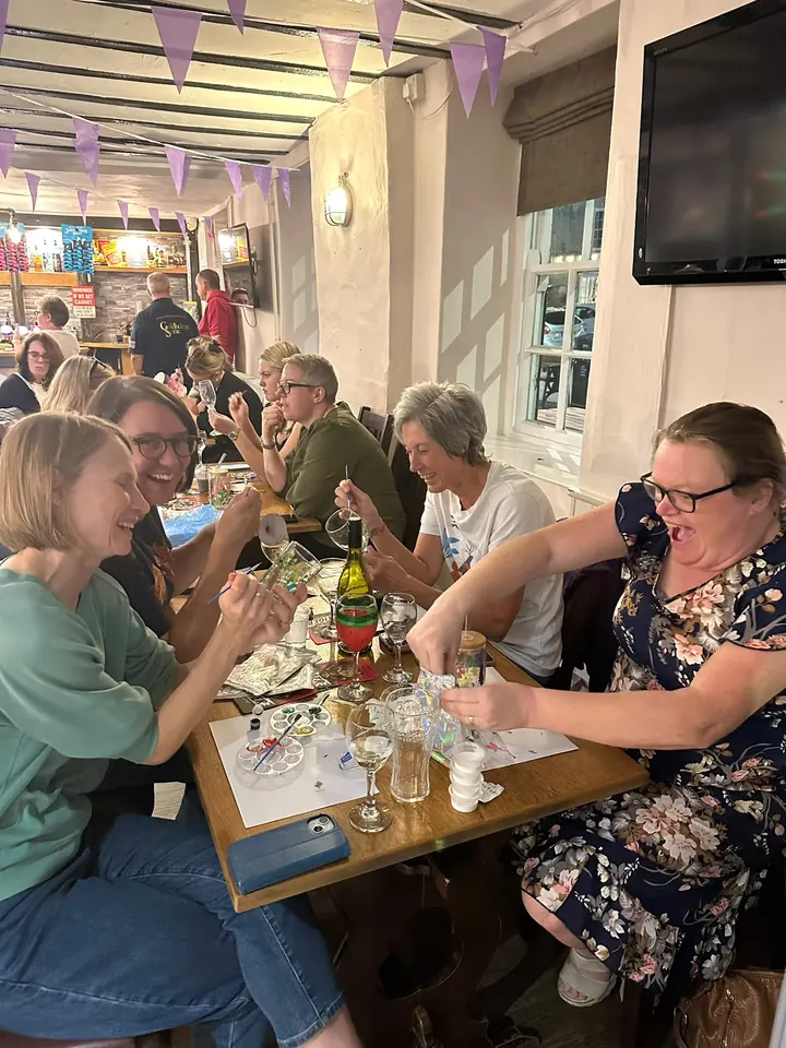 A table of guests laughing together as they paint glasses at a pub paint night