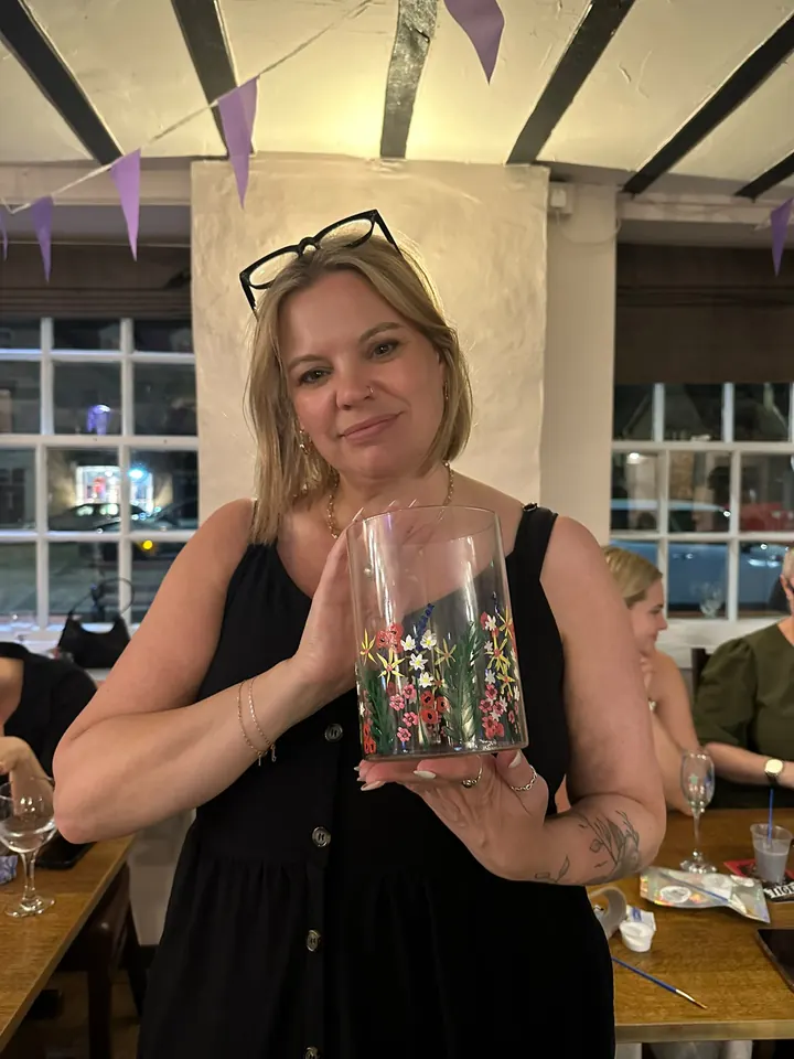 A guest holding up a glass vase she has painted with wildflowers